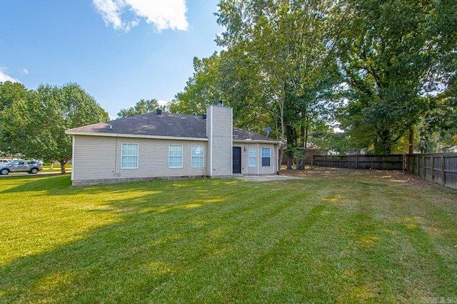 back of property featuring a chimney, fence, and a yard