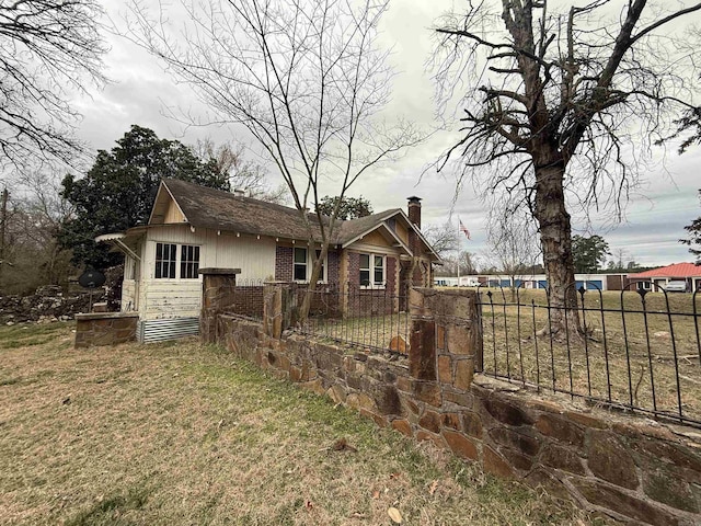 view of property exterior with a yard, a fenced front yard, a chimney, and brick siding