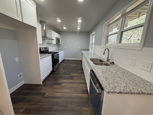 kitchen with dishwasher, wall chimney exhaust hood, light stone countertops, gas range oven, and a sink