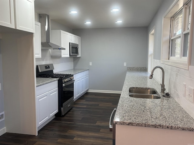 kitchen with dark wood-style floors, wall chimney exhaust hood, light stone countertops, stainless steel appliances, and a sink