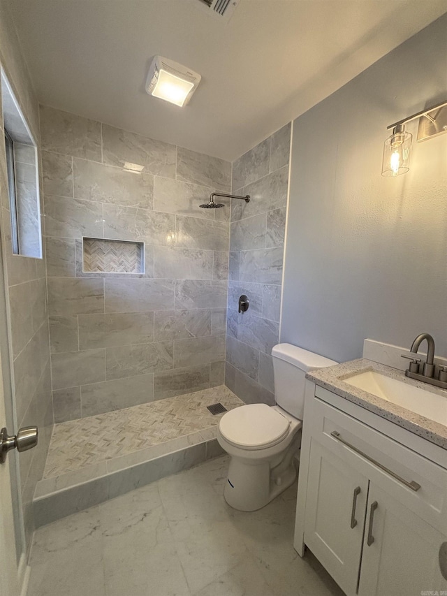 full bathroom with toilet, marble finish floor, tiled shower, and vanity