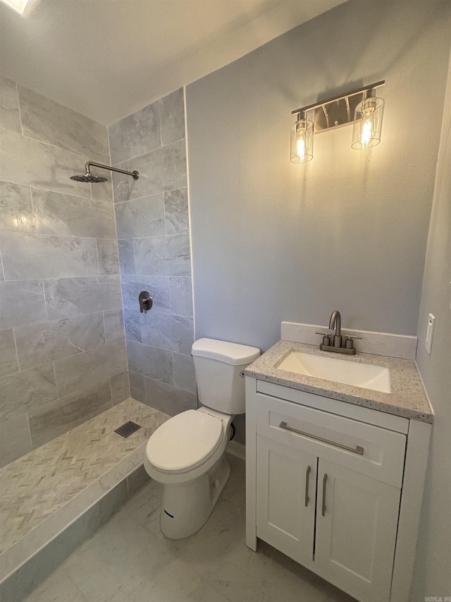 bathroom with toilet, marble finish floor, tiled shower, and vanity