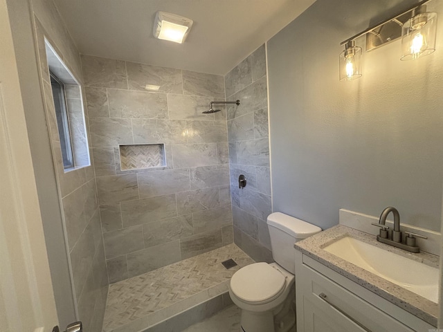 bathroom featuring a tile shower, vanity, and toilet