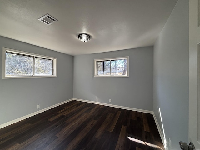 spare room featuring dark wood-style floors, visible vents, and baseboards