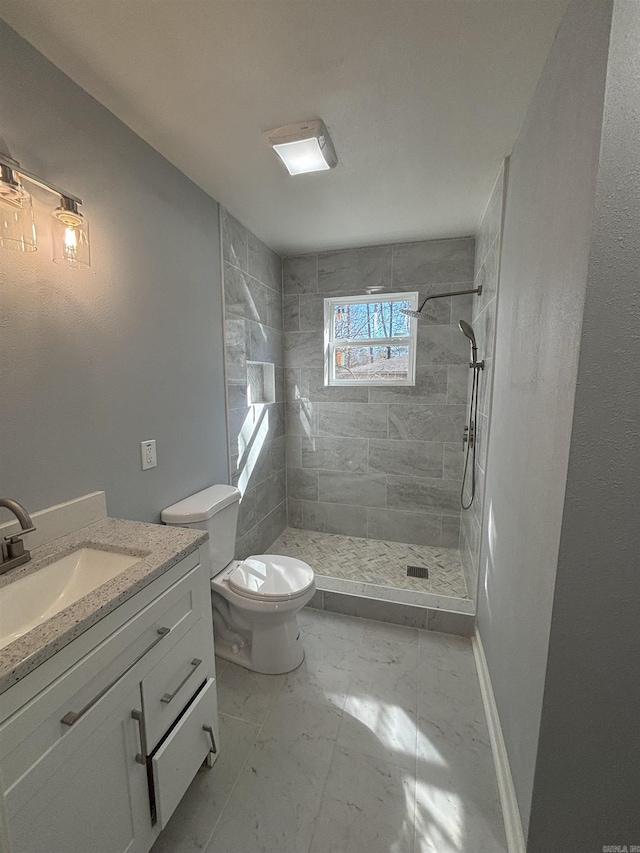 bathroom with marble finish floor, toilet, a tile shower, vanity, and baseboards