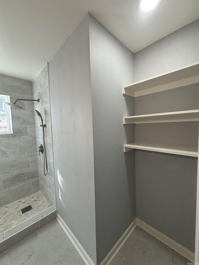 full bathroom with marble finish floor, tiled shower, and baseboards