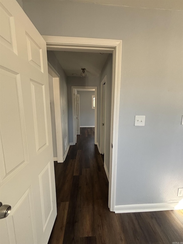 corridor with dark wood-style floors, visible vents, and baseboards