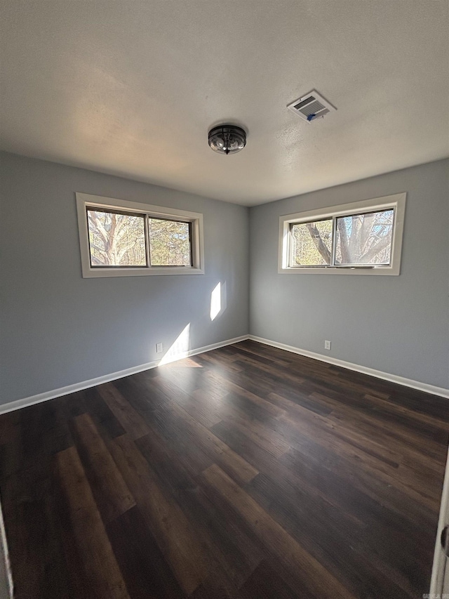 empty room with dark wood finished floors, visible vents, and baseboards