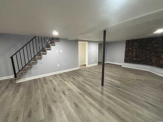 finished below grade area featuring stairway, baseboards, and wood finished floors