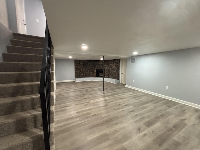 finished below grade area with a fireplace, wood finished floors, visible vents, baseboards, and stairway