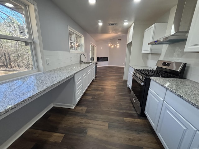 kitchen featuring light stone counters, visible vents, white cabinets, wall chimney range hood, and gas range