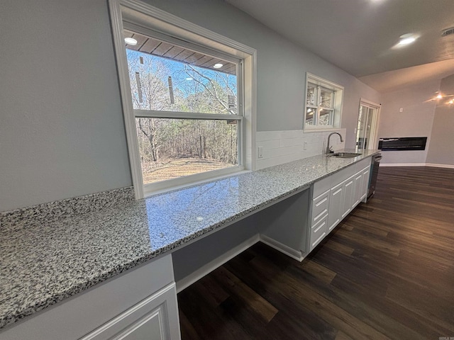 kitchen with dark wood-type flooring, a sink, white cabinets, backsplash, and light stone countertops