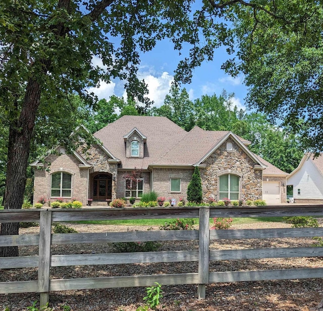 view of front of home featuring an attached garage, stone siding, a fenced front yard, and roof with shingles