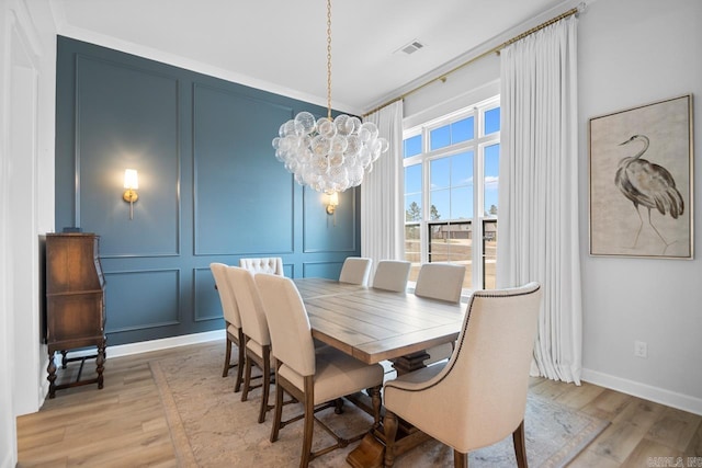 dining area featuring light wood-style floors, an inviting chandelier, visible vents, and a decorative wall