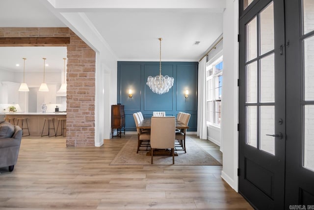 dining area featuring a decorative wall, french doors, light wood finished floors, an inviting chandelier, and crown molding