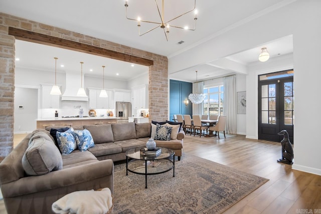 living room featuring baseboards, visible vents, ornamental molding, wood finished floors, and a notable chandelier