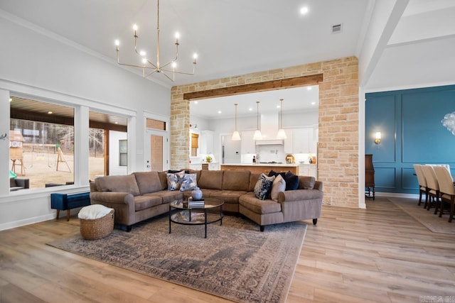 living area with crown molding, visible vents, a decorative wall, light wood-style floors, and a chandelier