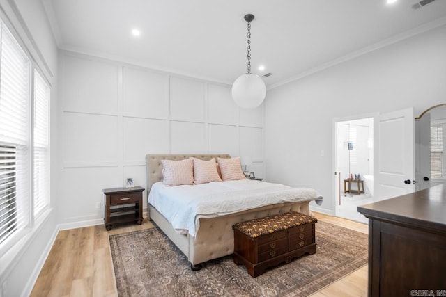 bedroom with light wood-style floors, multiple windows, a decorative wall, and crown molding