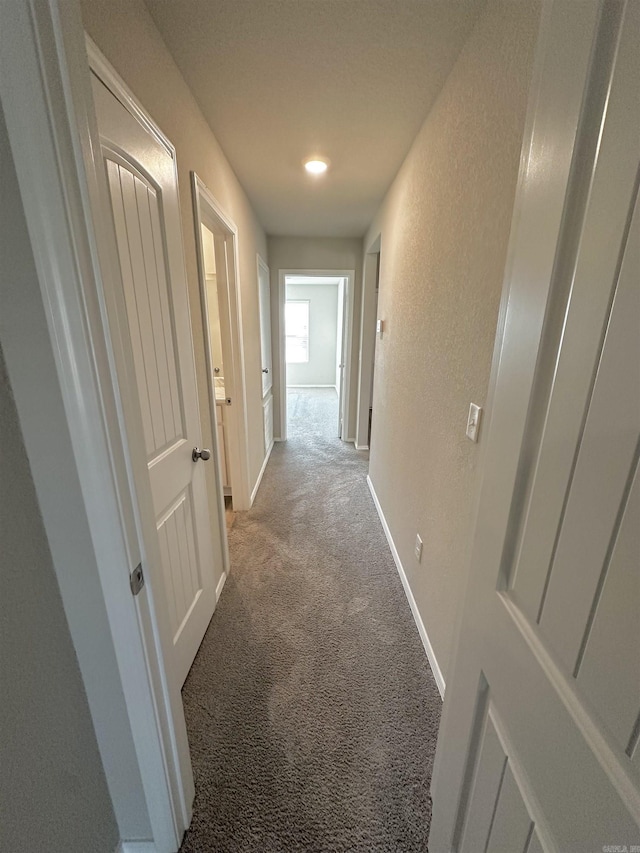 hallway featuring a textured wall, carpet flooring, and baseboards