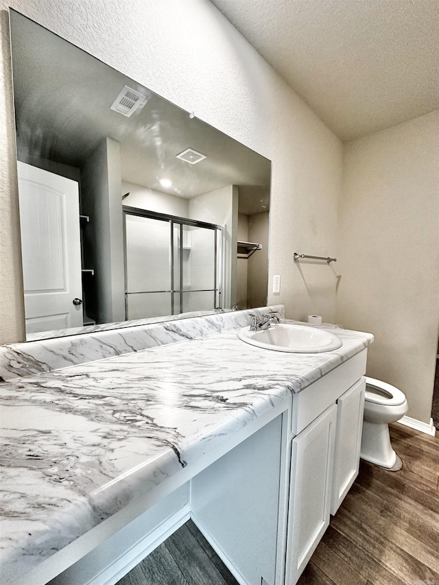 full bathroom featuring a stall shower, visible vents, toilet, wood finished floors, and vanity