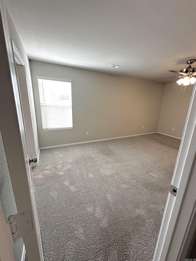 empty room featuring a textured ceiling, carpet, a ceiling fan, and baseboards