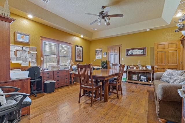 dining room featuring light wood-style flooring, a raised ceiling, a textured ceiling, and a textured wall