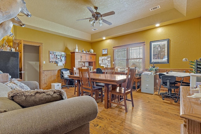 dining area with visible vents, a ceiling fan, a wainscoted wall, a textured ceiling, and light wood-type flooring