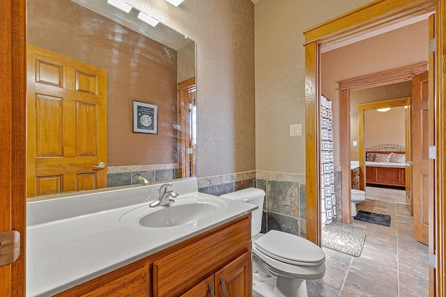 full bath featuring toilet, a textured wall, connected bathroom, and vanity