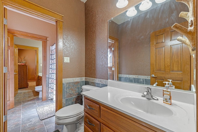 full bath with a textured wall, toilet, stone tile flooring, vanity, and tile walls