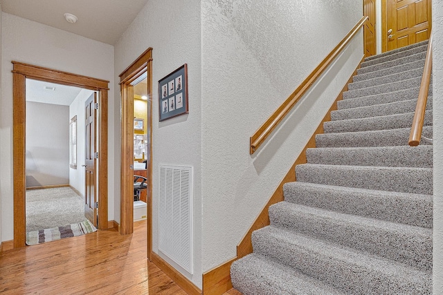 stairs featuring baseboards, visible vents, wood finished floors, and a textured wall