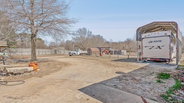 view of yard featuring a carport, fence, and dirt driveway