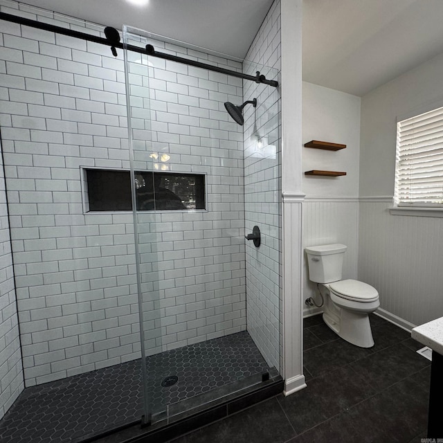 bathroom featuring a wainscoted wall, tile patterned flooring, toilet, and a shower stall