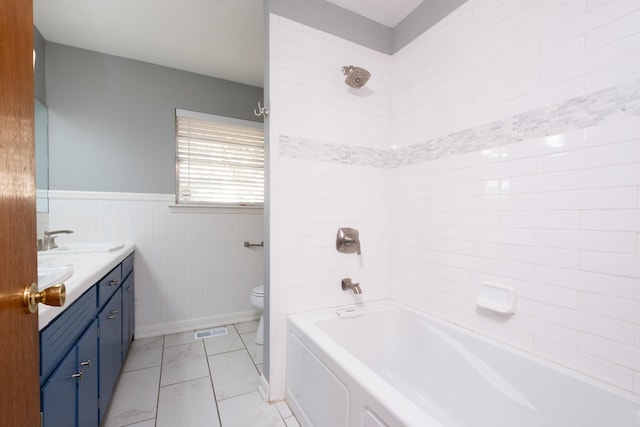 bathroom featuring double vanity, visible vents, toilet, a wainscoted wall, and a sink