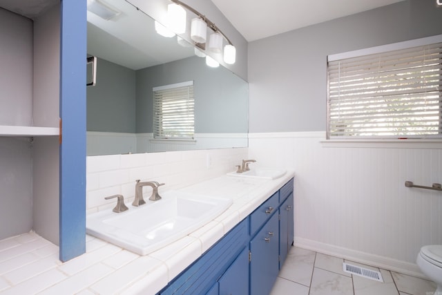 full bath with double vanity, wainscoting, a sink, and visible vents