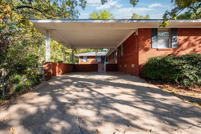 view of parking with driveway, an attached carport, and fence