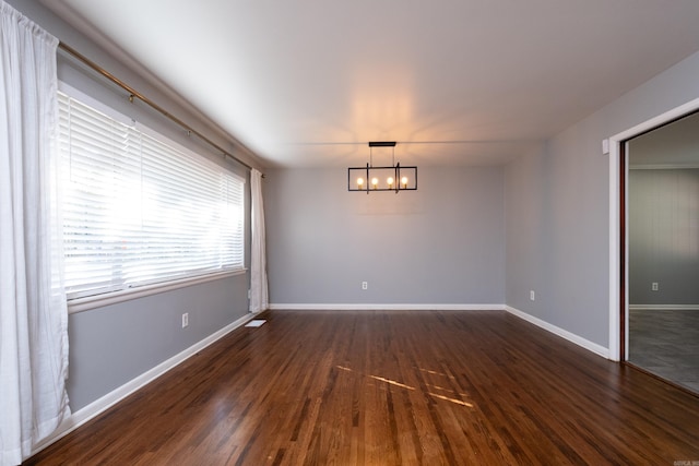 empty room with dark wood finished floors, baseboards, and an inviting chandelier