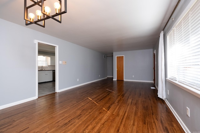 unfurnished room with a sink, baseboards, a chandelier, and dark wood-type flooring