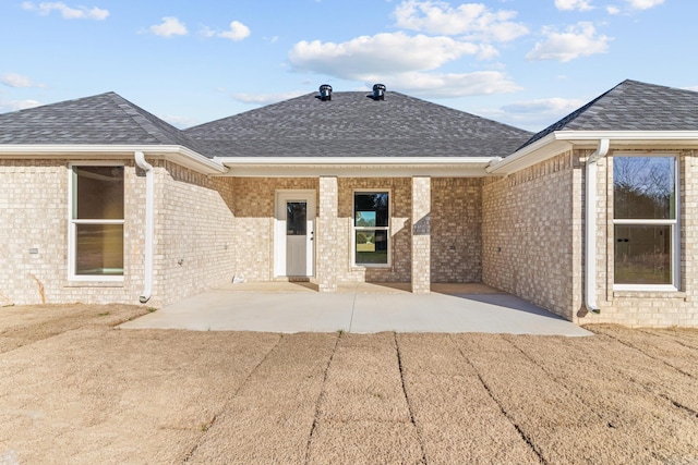 rear view of house with a patio, brick siding, and roof with shingles