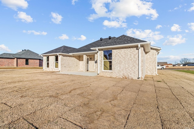 back of property with a patio area, a shingled roof, and brick siding