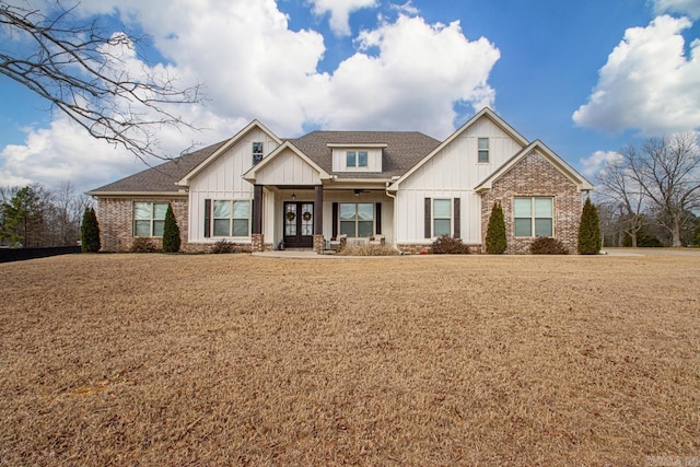 view of front facade with a shingled roof, a front lawn, board and batten siding, and brick siding