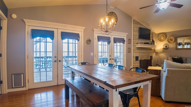 dining space featuring lofted ceiling with beams, ceiling fan, a stone fireplace, wood finished floors, and french doors