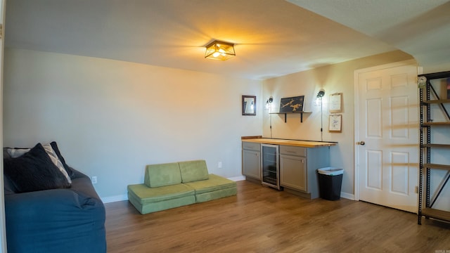 living area with beverage cooler, a dry bar, wood finished floors, and baseboards