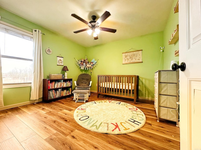 bedroom with a ceiling fan, a crib, baseboards, and wood finished floors