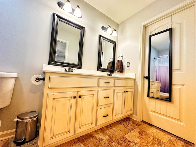 bathroom featuring stone finish flooring, baseboards, toilet, and double vanity