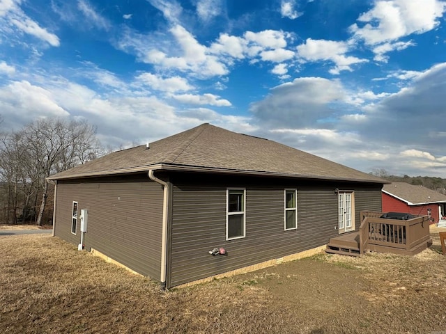 view of side of home with a deck and roof with shingles