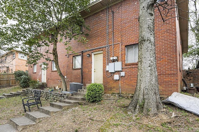 view of front facade with cooling unit, brick siding, and fence