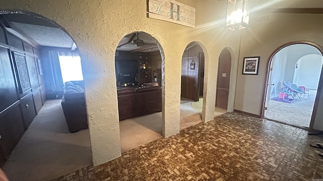 hall with arched walkways, a textured wall, and a textured ceiling