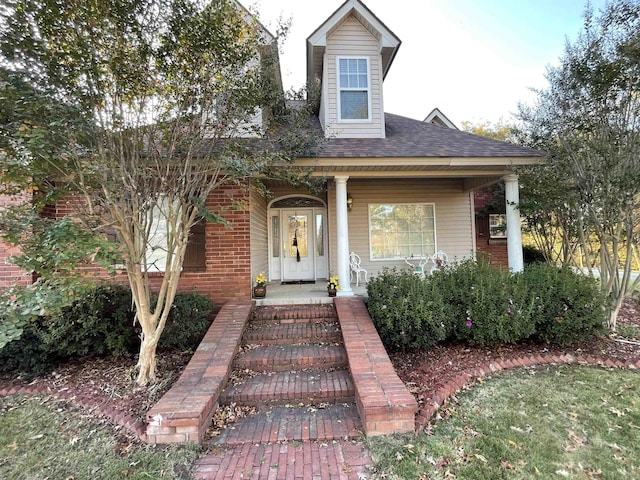 view of front of home featuring covered porch, roof with shingles, and brick siding