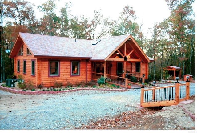 log-style house featuring a shingled roof, a porch, and log exterior