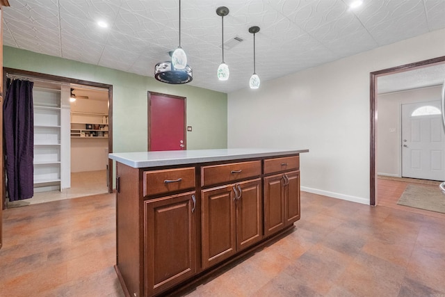 kitchen with light countertops, hanging light fixtures, visible vents, a kitchen island, and baseboards